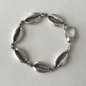 Jai Style simple, elegant, 7.5" handmade solid sterling silver cowrie shell bracelet with Jai Style embossed charm. Our cowrie shell bracelet represents goddess protection connected with the strength of the ocean.