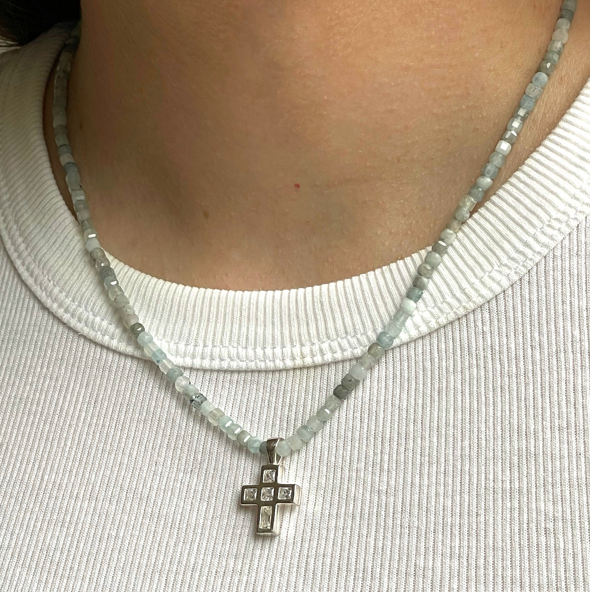 Beautiful, handcrafted 3mm square cut faceted Aquamarine semi-precious stone necklace with sterling silver and cubic zirconia cross charm; elegant on its own and perfect for layering; adorned with .925 sterling silver Jai Style hand-embossed charm and lobster clasp; 18" length.