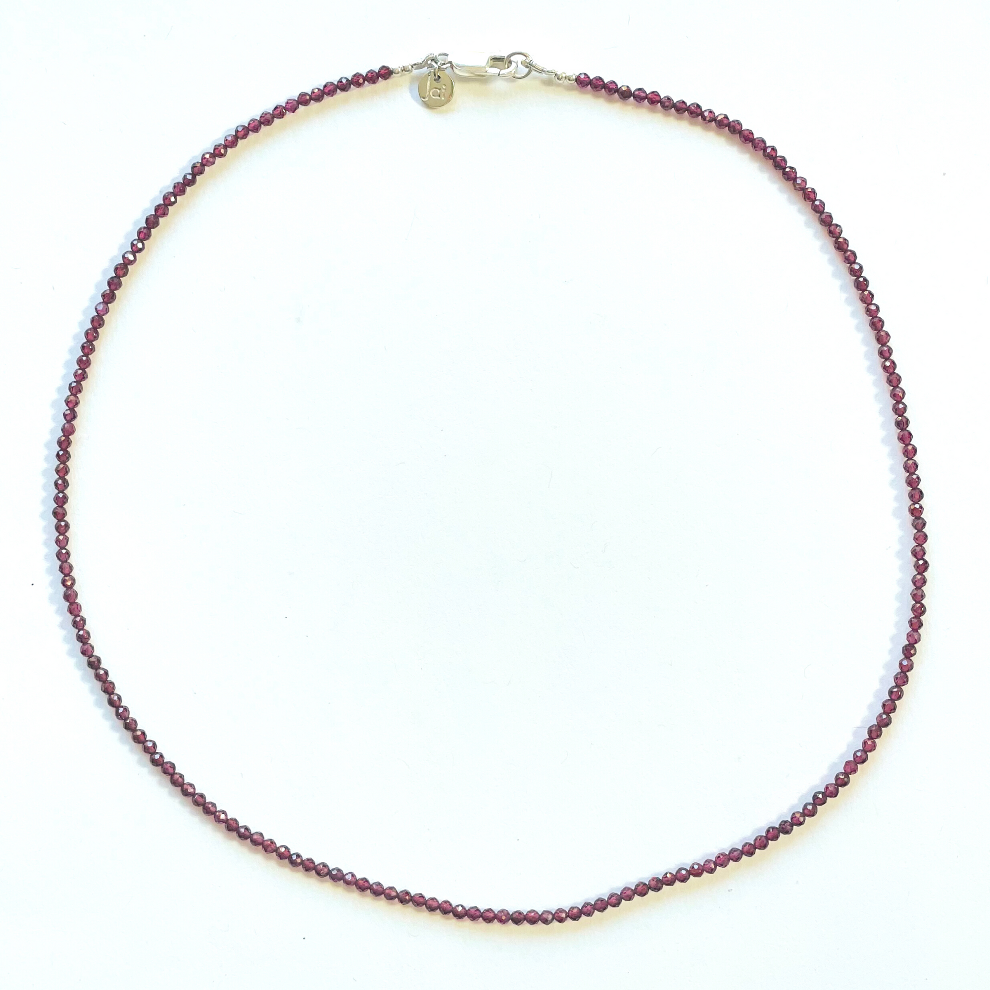 Beautiful, handcrafted 2mm round faceted Garnet semi-precious stone necklace; elegant on its own or with a pendant/charm, and perfect for layering; adorned with .925 sterling silver Jai Style hand-embossed charm and lobster clasp; necklace measures 16".