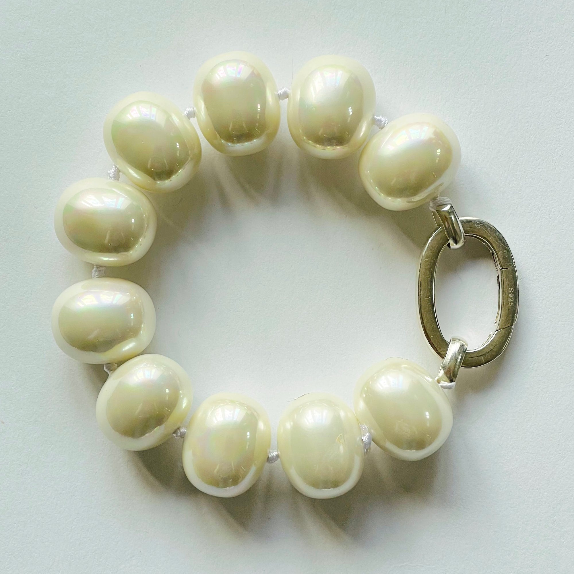 Beautiful handcrafted cuff-style statement bracelet of organic white freshwater shell pearls, approx. 19 m x 11 mm. Hand-knotted with white thread, bracelet measures 21 cm (8.25 in.). Elegant on its own and perfect with a charm or two. Adorned with .925 sterling silver oval clasp.