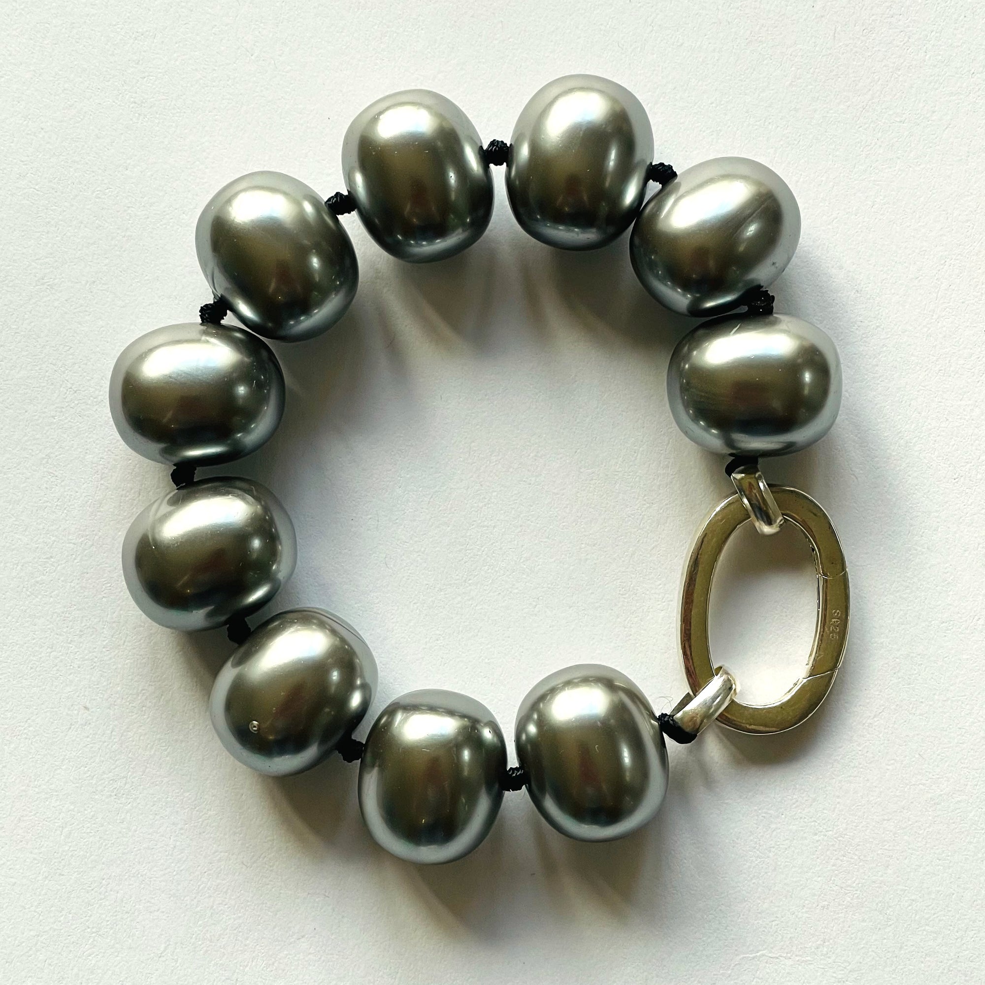 Beautiful handcrafted cuff-style statement bracelet of organic silver freshwater shell pearls, approx. 19 m x 11 mm. Hand-knotted with black thread, bracelet measures 21 cm (8.25 in.). Elegant on its own and perfect with a charm or two. Adorned with .925 sterling silver oval clasp.